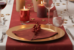 Festliche Weihnachts-Tischdeko in Gold und Weiß: Platzteller, Stoffservietten, Besteck und Lichterkette.