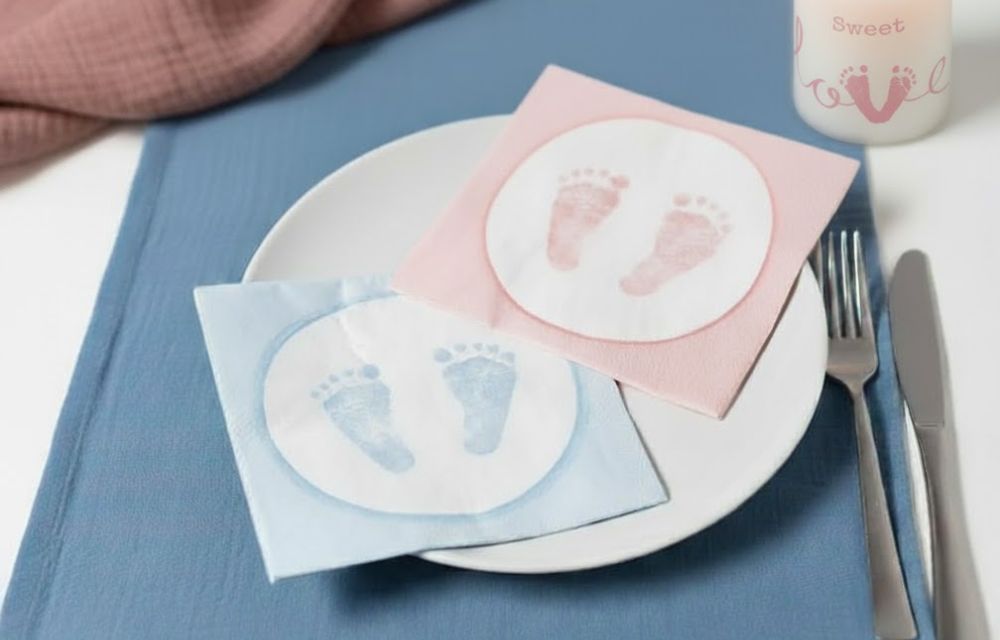Süße Tischdeko zur Taufe mit rosa und hellblauen Servietten, die Baby-Fußabdrücke auf einem Teller abbilden.