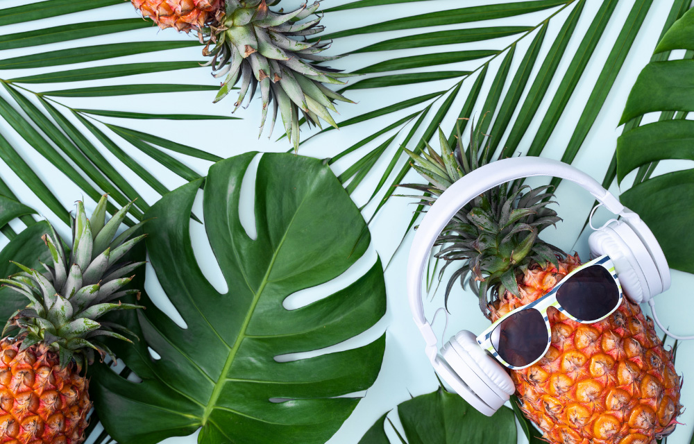 Kreative Tischdeko-Idee: coole Ananas mit Kopfhörern und Sonnenbrille auf Monstera-Blättern für eine tropische Gartenparty.