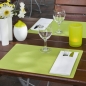 Holz Tisch in Dunkelbraun mit grünen Platzsets, weißen Bestecktaschen, Kerzenschein und weißem Vasen mit Blumen.