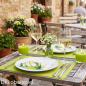Frühlingshaft gedeckter Tisch im Freien mit grünen Platzsets, Spargel-Servietten, Kerzenschein und weißem Blumenschmuck.