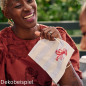 Eine fröhliche Frau mit sommerlichem Outfit im Freien hält eine maritime Hummer-Serviette der Duni Serie Sea Delights n der Hand..